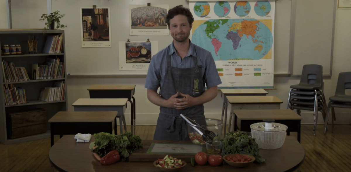 preson standing in classroom with vegetables on the table.